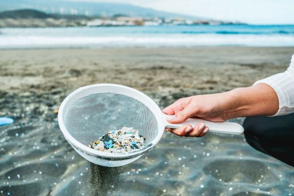 Young woman cleaning microplastics from sand on the beach - Environmental problem, pollution and ecolosystem warning concept - Focus on hand