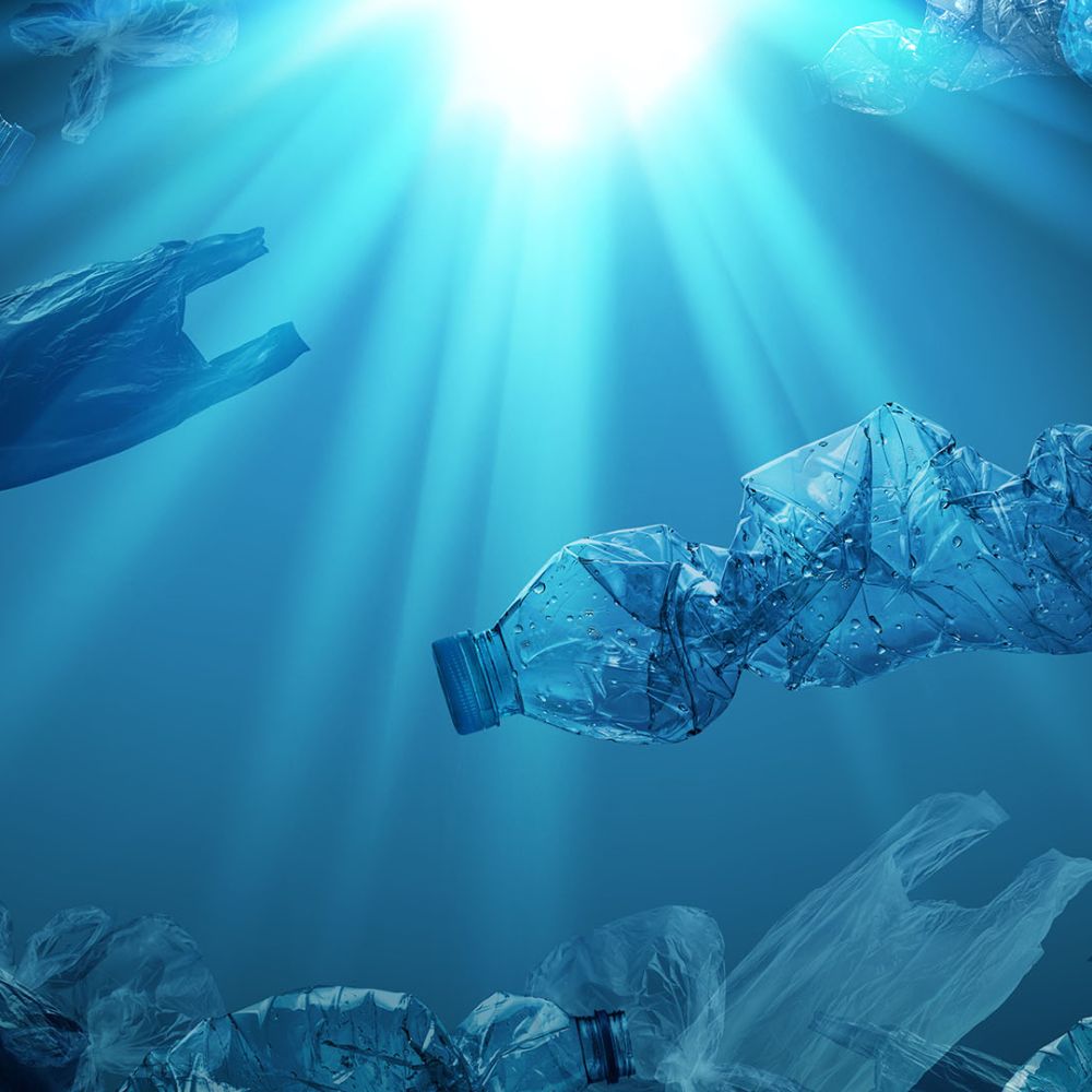 creative background of PET plastic bottles and single-use plastic bags floating in sea or ocean with rays of sunlight effect, polyethylene terephthalate plastic, concept of environmental pollution.